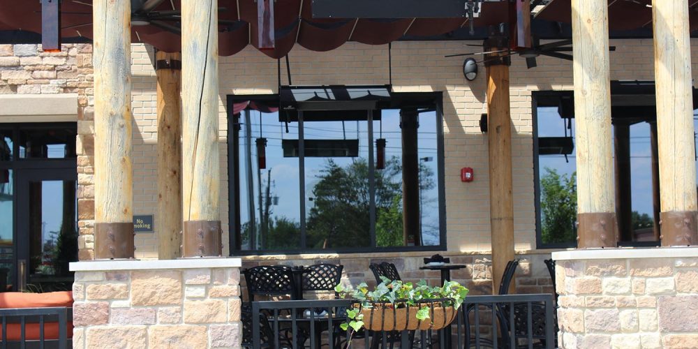 Exterior view of outdoor dining section of Fire Birds; large dark plate glass windows visible